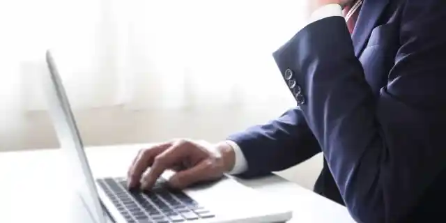 スーツ姿でノートパソコンを操作している人の写真